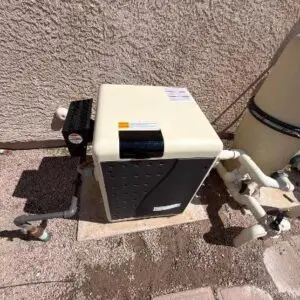 Outdoor pool equipment: a beige cabinet pump/heat unit on a concrete pad with connected pipes and a filter beside it against a stucco wall.