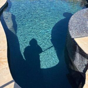 Shadow of two people holding hands cast on the surface of a sunlit blue pool near the edge.