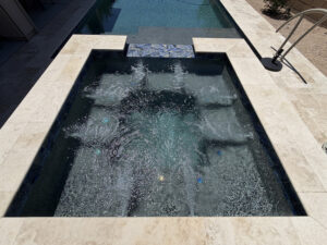 Rectangular outdoor spa with bubbling jets and stone coping, next to a larger swimming pool.
